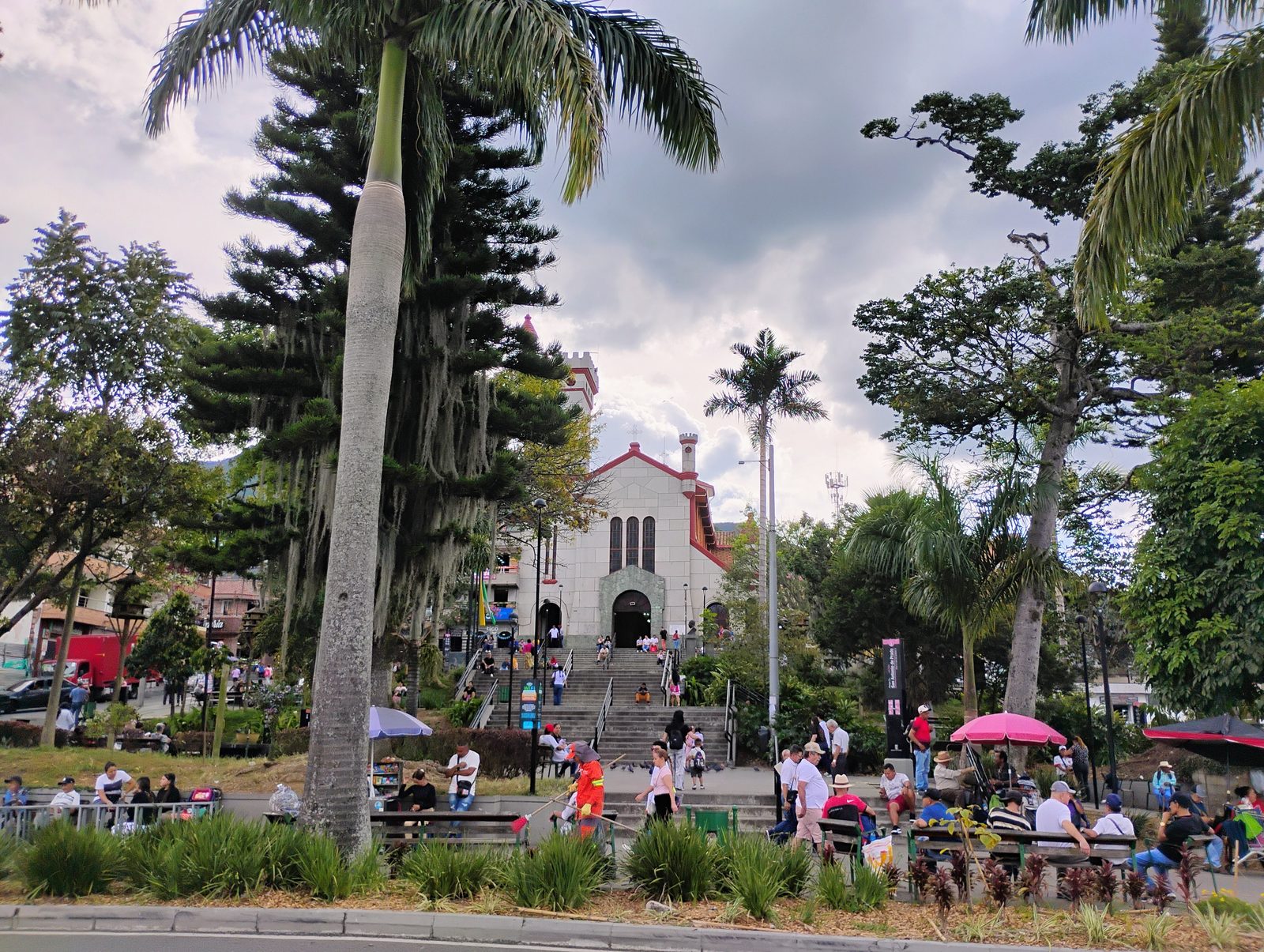 El parque principal de San Antonio de Prado, con palmas y pinos y el templo al fondo.